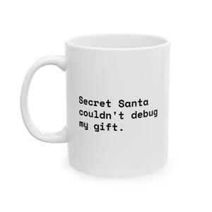 Könnte beinhalten: Ein weißer Keramikbecher mit einem geschwungenen Henkel und dem schwarzen Aufdruck: Secret Santa couldn't debug my gift. Der Becher hat einen glatten, zylindrischen Körper und ein schlichtes Design für den täglichen Gebrauch als Trinkgefäß.