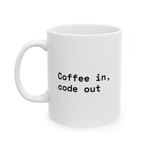 Puede incluir: Una taza de cerámica blanca con un asa curva que presenta el texto negro Coffee in, code out impreso en el lateral. La taza tiene un cuerpo cilíndrico liso y un diseño sencillo y funcional para contener bebidas calientes o frías.