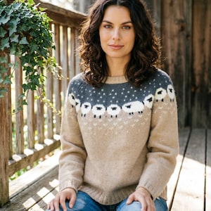 May include: A long-sleeved knit sweater featuring a tan base color with a dark gray yoke. The yoke is decorated with a repeating pattern of white sheep figures and small white dots. The sweater has a round neckline and ribbed cuffs and hem.