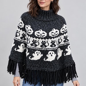 May include: A charcoal gray knit poncho featuring a high turtleneck collar and long black fringe along the hem. The garment displays a repeating white jacquard pattern of jack-o'-lanterns, black cats, and ghosts arranged in horizontal bands.