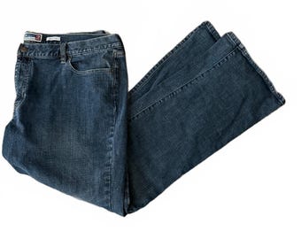 May include: Dark blue denim jeans featuring a flared leg silhouette, a classic five-pocket design, a button and zipper fly closure, and a visible brand label on the interior waistband. The fabric has a subtle faded wash throughout.