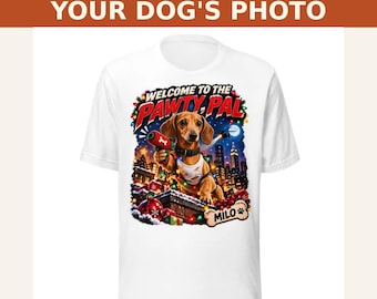 May include: A white t-shirt featuring a graphic of a dachshund wearing a white tank top and holding a red toy gun. The text reads "WELCOME TO THE PAWTY, PAL" and "MILO" on a bone-shaped sign. The background shows a city skyline with Christmas lights.