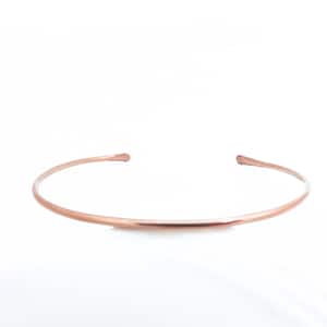 May include: A delicate, open-ended copper-coloured choker necklace. The minimalist design features a thin, curved band that gently tapers at the ends. The jewellery is set against a bright white background, highlighting its simple elegance.