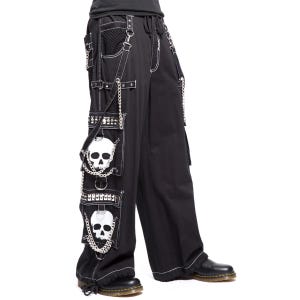 May include: Black wide-leg cargo pants featuring white contrast stitching, silver-tone metal chains, and studded straps. The side pockets are decorated with two large white skull graphics, metal D-rings, and additional silver chain embellishments.