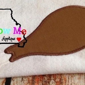 May include: A brown felt appliqué of a chicken leg with a white felt bone. The appliqué is on a white background with the text "Show Me Applique" in colourful letters.
