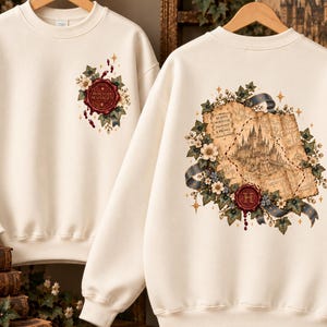 May include: An off-white crewneck sweatshirt featuring a front graphic of a red wax seal with the text Mischief Managed and a back graphic of a vintage map, a castle illustration, a red wax seal with the letter H, and floral accents.