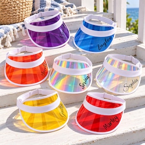 May include: Seven translucent plastic sun visors with white adjustable headbands. The visors come in purple, blue, orange, iridescent, yellow, and red colors. Each visor features a custom name printed in black script: Gracy, Zaylee, Yareli, Serina, Sophia, Gretta, and Marley.