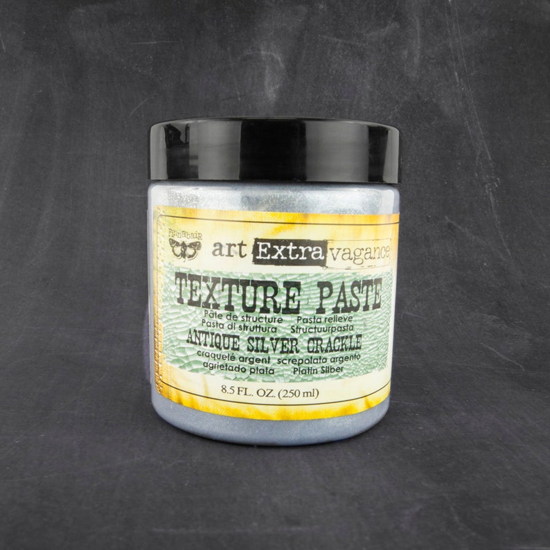 May include: A silver jar of texture paste labeled "art Extra vagance Texture Paste Antique Silver Crackle" with the text "P&ocirc;te de structure Pasta relieve Pasta di struttura Structuurpasta craquel&eacute; argent screpolata argento agrietado plata Platin Silber 8.5 FL. OZ. (250 ml)"