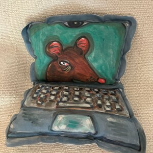 May include: A blue and gray pillow shaped like a laptop computer with a brown mouse peeking out of the screen. The screen is green and the mouse has red ears.