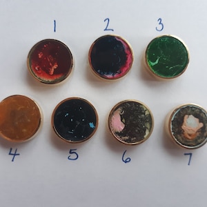 May include: Seven round, gold-rimmed buttons with different colorful designs. The buttons are numbered 1 through 7.