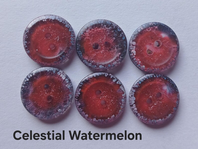 Puede incluir: Seis botones circulares dispuestos en dos filas de tres. Cada bot&oacute;n presenta un centro rojo intenso con una textura brillante y reluciente, rodeado por un borde oscuro y moteado con puntos blancos. El texto Celestial Watermelon est&aacute; debajo.