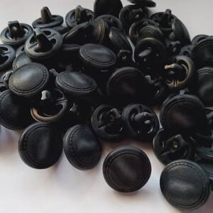 May include: A large pile of black plastic buttons with a raised, textured surface. The buttons have a two-hole design.