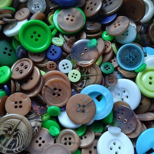 May include: A collection of various buttons in shades of green, brown, blue, and white. The buttons vary in size and shape, with four-hole and two-hole designs. Some buttons have a glossy finish, while others are matte.