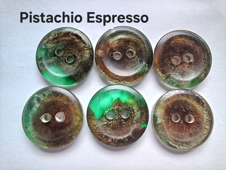 Puede incluir: Seis botones redondos con dos agujeros cada uno, que presentan una mezcla arremolinada de colores verde transl&uacute;cido y marr&oacute;n oscuro. El texto 'Pistachio Espresso' est&aacute; impreso en negro sobre los botones, que tienen un acabado liso, brillante y semitransparente.