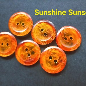 Puede incluir: Seis botones redondos con un patr&oacute;n jaspeado de color &aacute;mbar y naranja transl&uacute;cido, cada uno con dos agujeros centrales. El texto Sunshine Sunset est&aacute; impreso en amarillo sobre los botones. Los botones tienen un acabado liso y brillante.
