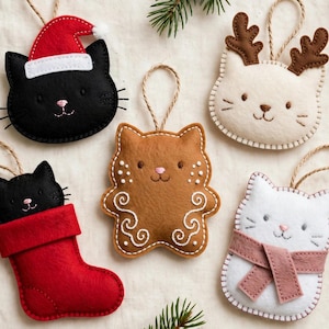 Pode incluir: Cinco enfeites de feltro em forma de gato com laços de juta para pendurar. Um gato preto usa um gorro de Pai Natal vermelho, um gato branco tem chifres de feltro castanhos, um gato preto está numa meia vermelha, um gato castanho tem bordados brancos e um gato branco usa um cachecol rosa.
