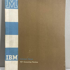 Może przedstawiać: Brązowy podręcznik referencyjny IBM 407 Accounting Machine z pionowym niebiesko-białym szachownicowym grzbietem. Okładka zawiera literę M na górze, logo IBM na dole oraz tekst Reference Manual 407 Accounting Machine.