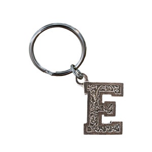 May include: Silver keychain with a decorative letter E charm. The letter is surrounded by a floral design.