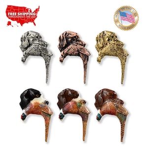 May include: Six different colored metal pins depicting a dog carrying a pheasant. The pins are in silver, copper, gold, black, brown, and red. The pins are all in the same pose, with the dog's head turned to the side and the pheasant in its mouth. The pins are all about 2 inches tall.