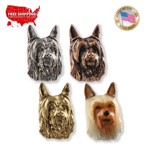 May include: Four different colored metal pins of a Yorkshire Terrier dog breed. The pins are silver, copper, gold, and white with brown accents.