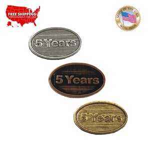 May include: Three oval-shaped metal pins with the text "5 Years" engraved on them. The pins are silver, copper, and gold.