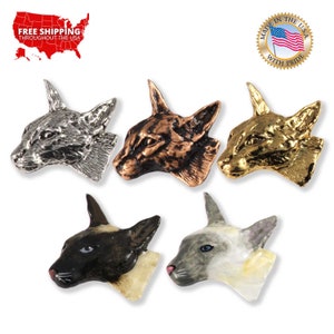May include: A collection of cat-shaped decorative pins in various metallic finishes, including silver, bronze, and gold. Two pins feature painted cat faces with black, white, and gray markings. The pins are displayed on a white background.