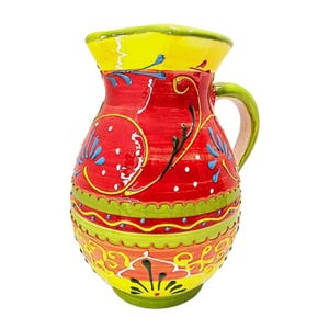 May include: A ceramic pitcher featuring a vibrant red body with a yellow rim and base. The surface is decorated with hand-painted blue and green floral motifs, swirling lines, and white dots, complemented by a curved green handle on the side.