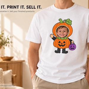 May include: A white short-sleeved t-shirt featuring a graphic of a cartoon pumpkin character with a child's face inserted into the pumpkin head. The character wears a black outfit, holds a purple jack-o'-lantern bucket, and waves a hand.