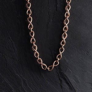 Puede incluir: Un collar de cadena en oro rosa que presenta una serie de eslabones interconectados con forma de símbolo de infinito. Los eslabones metálicos son uniformes en tamaño y forma, creando un patrón continuo y repetitivo en toda la pieza.