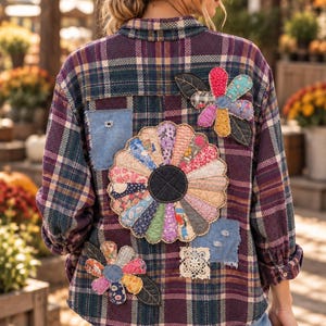May include: A long-sleeve button-down shirt in a dark purple, green, and tan plaid pattern. The back features multiple fabric flower appliqués made from various colorful patterned textiles, along with small denim and lace patches.