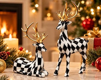 May include: Two ceramic deer figurines featuring a black and white diamond harlequin pattern on their bodies and metallic gold antlers. One deer is depicted in a reclining position, while the other deer stands upright on a smooth surface.