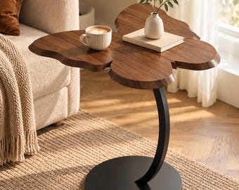 May include: A side table with a dark brown wood top shaped like a butterfly, supported by a curved black metal stem and a circular black base. A white ceramic mug and a small white vase on a book are placed on the table surface.