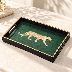 May include: A rectangular serving tray with a black exterior and a gold-toned rim. The interior features a dark green surface with a herringbone pattern and a central illustration of a walking leopard in shades of gold and white.