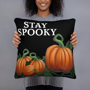 May include: Black decorative pillow with the words "STAY SPOOKY" in white. The pillow features orange pumpkins with green vines and leaves, perfect for Halloween decor.