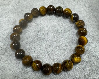 May include: A circular beaded bracelet composed of polished tiger's eye gemstones. The beads feature alternating bands of golden-brown and dark brown colours with a chatoyant lustre, arranged in a continuous loop on an elastic cord.