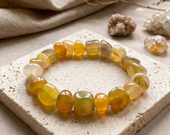 May include: A stretch bracelet composed of polished, tumbled gemstone beads in various shades of yellow, amber, and golden honey. The beads are smooth, rounded, and translucent, creating a continuous circular loop of warm, earthy tones.