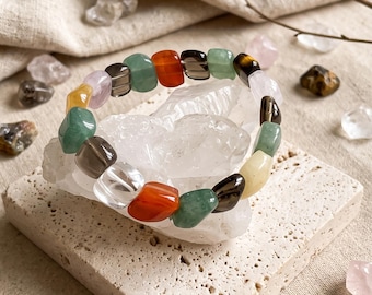 May include: A stretch bracelet composed of polished, irregular tumbled gemstone beads in various colours including green, orange, brown, yellow, clear, and light pink, arranged in a circular pattern around a central clear quartz cluster.