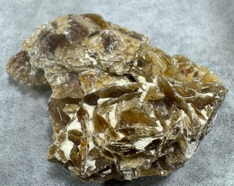 May include: A raw, unpolished mineral specimen featuring a cluster of translucent, amber-brown crystalline formations with jagged, layered edges and opaque, off-white mineral deposits embedded between the sharp, angular crystal plates.