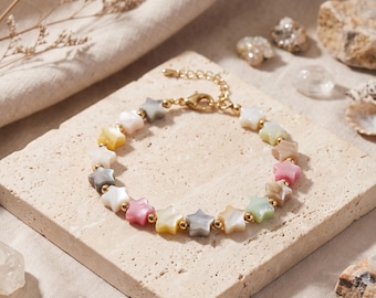 May include: A bracelet featuring a series of small, multi-coloured star-shaped beads made of iridescent material, interspersed with tiny gold-toned metal spheres. The bracelet includes a gold-toned lobster claw clasp and an adjustable chain link.