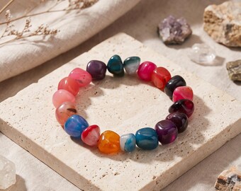 May include: A stretch bracelet composed of smooth, tumbled, multi-coloured gemstone beads in shades of red, orange, blue, purple, and pink. The beads are rounded and polished, arranged in a circular pattern to form a flexible wrist accessory.