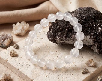 May include: A circular bracelet composed of smooth, translucent white crystal beads. The beads are uniform in size and strung together to form a continuous loop, showcasing a clear, polished surface that reflects light across the spherical shapes.
