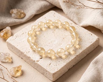 May include: A circular bracelet composed of faceted, translucent yellow citrine beads strung together. The beads are round and polished, reflecting light across their multiple cut surfaces, creating a bright, golden appearance.