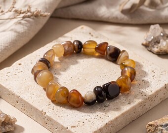 May include: A stretch bracelet composed of polished, irregular tumbled gemstone beads in various shades of amber, brown, tan, and translucent cream. The beads are smooth and rounded, featuring natural colour variations and banding patterns throughout the circular arrangement.