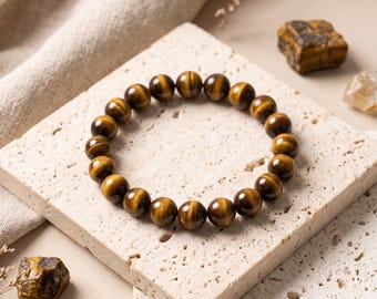 May include: A circular stretch bracelet composed of polished, spherical tiger's eye beads. The beads exhibit a characteristic chatoyant lustre with alternating bands of golden-brown and dark brown colours, arranged in a continuous loop.