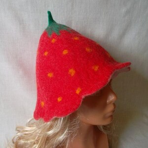 May include: A whimsical strawberry-shaped hat. The hat is primarily red with small yellow dots, mimicking the appearance of a ripe strawberry. The stem and leaves are green. The hat is made of felt.