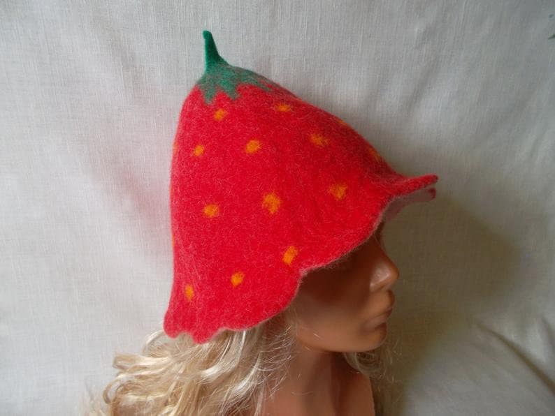 May include: A whimsical strawberry-shaped hat. The hat is primarily red with small yellow dots, mimicking the appearance of a ripe strawberry. The stem and leaves are green. The hat is made of felt.