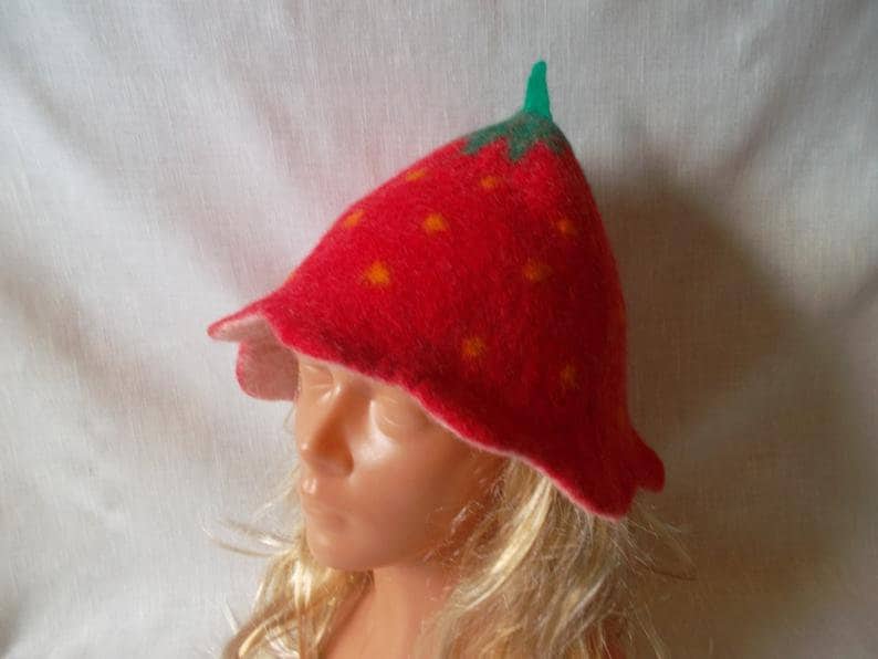 May include: A whimsical red felt hat shaped like a strawberry, complete with green stem and yellow seed details. The hat has a flared brim and is designed to be worn. A fun and unique accessory.