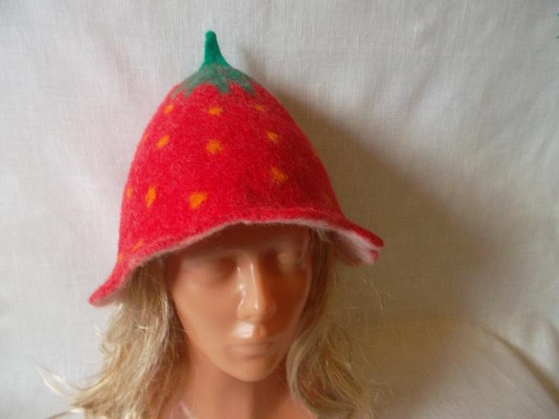 May include: A whimsical red felt hat shaped like a strawberry, featuring a green stem and small orange seeds. The hat has a flared brim and is designed to resemble the fruit. The hat is a fun accessory.
