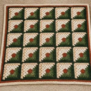 May include: A square crochet blanket featuring a repeating pattern of twenty-five blocks. Each block is composed of cream, light green, dark green, and rust-colored yarn, arranged in a geometric design with a central rust-colored flower motif.