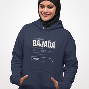 May include: A navy blue hooded sweatshirt featuring a white graphic print on the chest. The text reads BAJADA, followed by a dictionary-style definition, phonetic pronunciation, and the phrase IT WAS OUT, with a small yellow circle accent.